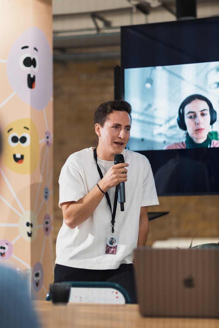 A young adult presenting with a microphone in a modern office setting.